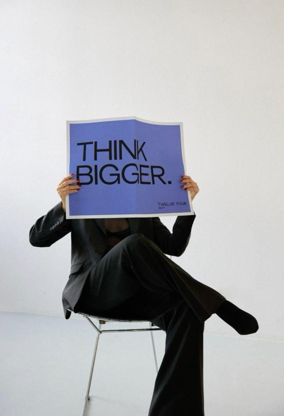 Person holding a sign with 'THINK BIGGER.' text against a white background
