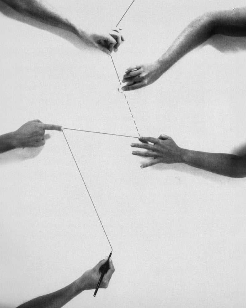 Black and white photo of multiple hands holding a kite string against a plain background