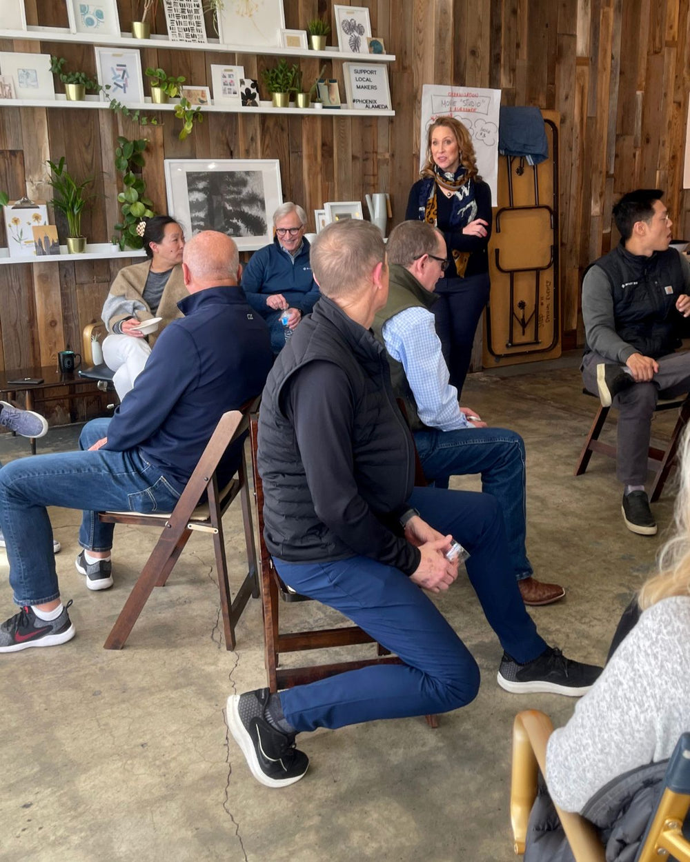Group of people sitting in a circle in a rustic room with wooden walls and shelves.